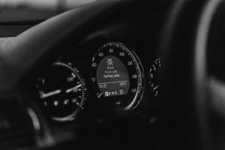 Close-up of a car dashboard in black and white with a parking lamp warning light.