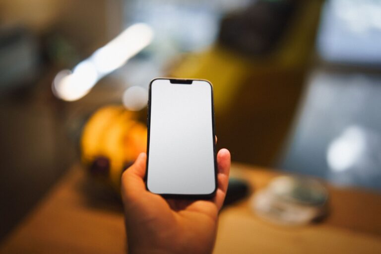 A person holding a smartphone with a blank screen, ideal for mockup use in an indoor setting.