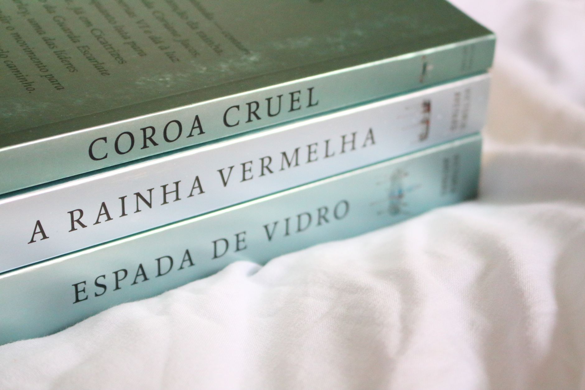Three novels with Portuguese titles neatly stacked on a soft white background.
