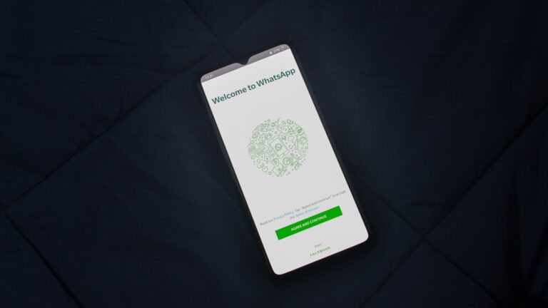 Smartphone displaying WhatsApp login screen on a dark surface. Overhead view.