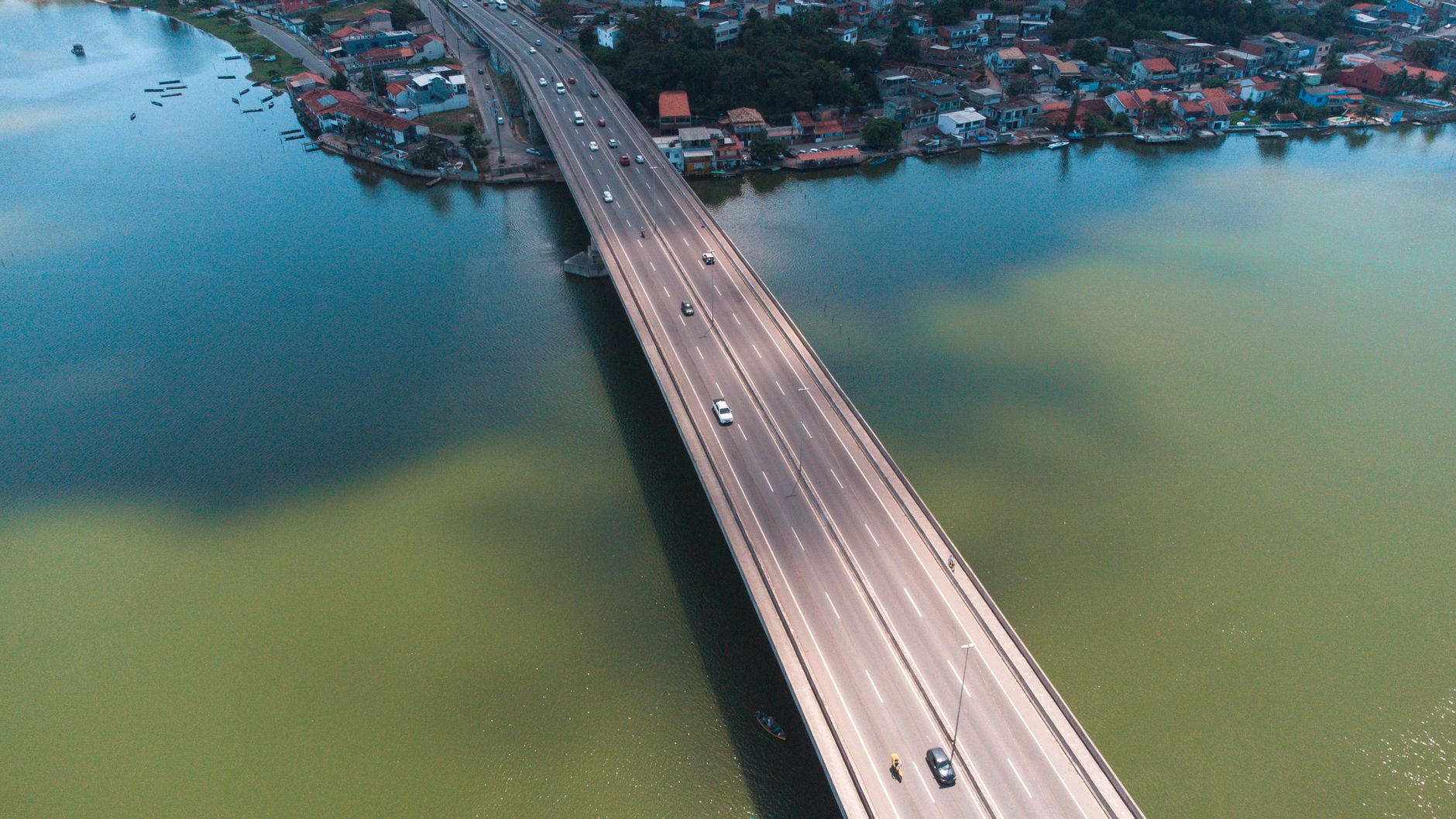 An aerial shot of a highway bridge crossing a tranquil lake with vehicles in motion and a picturesque town nearby.